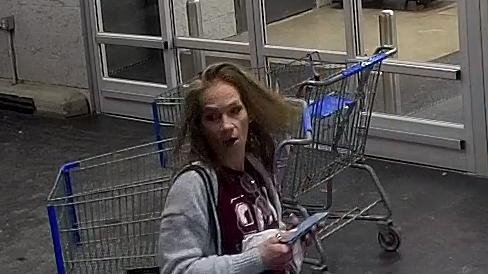 A woman with long hair holding a magazine near shopping carts at a store entrance.