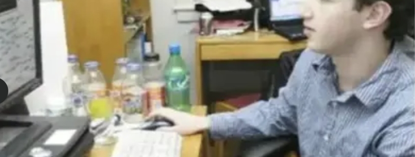 Fostoria News Young man working at a computer in a dorm room setting.