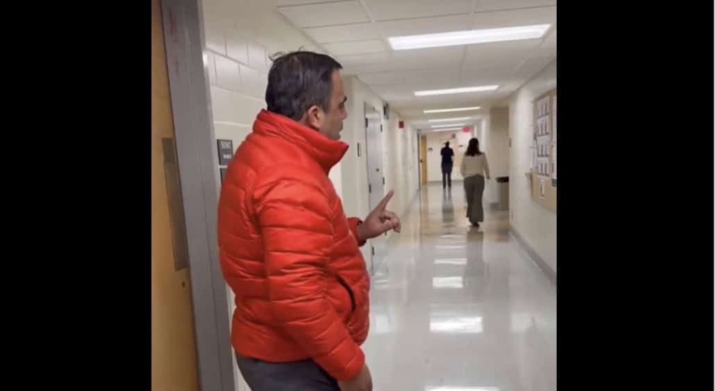 Fostoria News Man in red jacket gesturing in school hallway during confrontation.