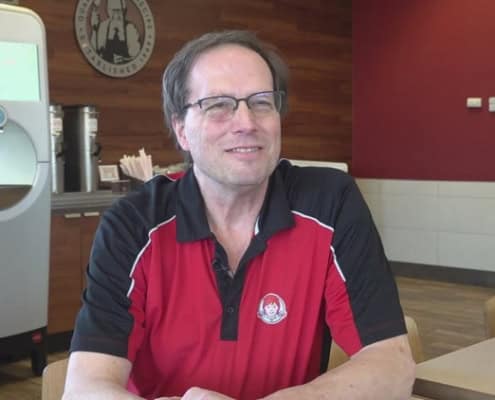 A man in a red and black polo shirt smiling at the camera inside The Fostoria Free Press office.