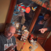 Man using phone in restaurant with people pointing and taking photos.
