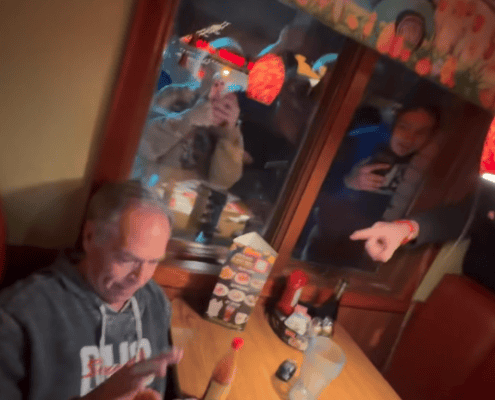 Man using phone in restaurant with people pointing and taking photos.