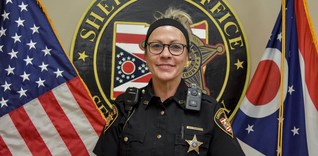Sheriff's officer in front of sheriff's office seal with American and Ohio flags.
