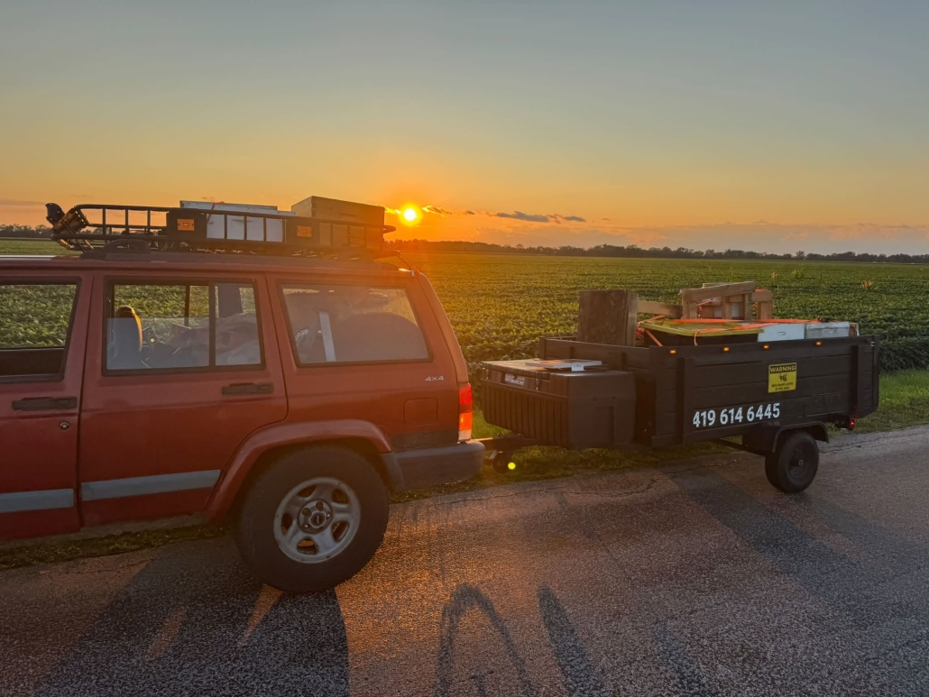 Red vehicle with honeybee removal equipment at sunset in rural area.