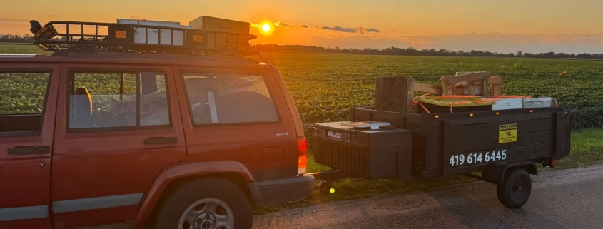 Red vehicle with honeybee removal equipment at sunset in rural area.