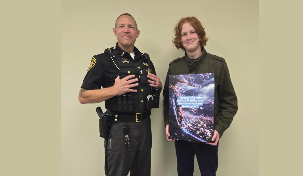 Fostoria News Police officer and young man holding a book together in an indoor setting.
