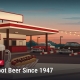 Fostoria News Vintage-style root beer stand with cars and string lights at sunset.
