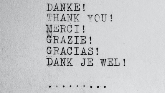 Typed text on white paper says "DANKE! THANK YOU! MERCI! GRAZIE! GRACIAS! DANK JE WEL!" followed by a row of dots.