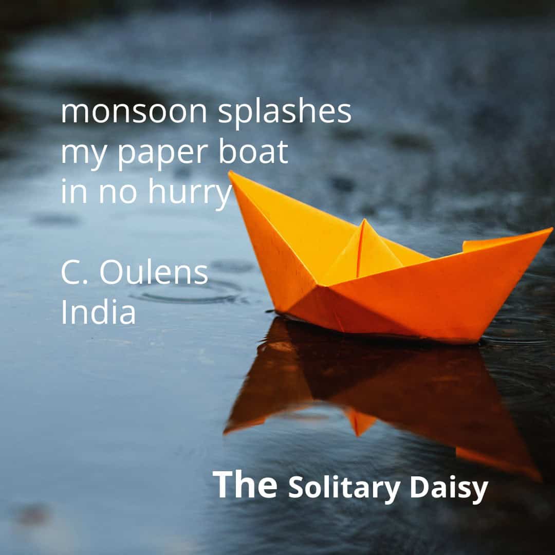An orange paper boat floats on a rain-soaked surface. Text on the image shows a haiku about a monsoon and the poet’s name, C. Oulens, along with “India” and “The Solitary Daisy.”.