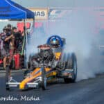 V8 drag racing car performing burnout at Titan Speed Engineering event with team members and spectators in the background.