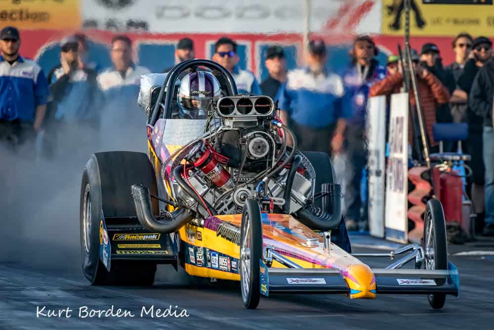Highly detailed drag racing car engine at Titan Speed Engineering, showcasing high-performance automotive engineering and speed, with a blurred crowd in the background.