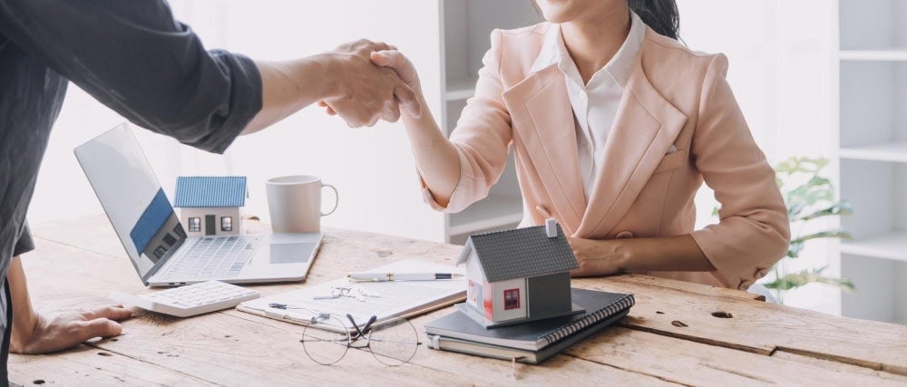 Real estate agent and client handshake over house model, property sales, home buying, real estate negotiation, professional service.