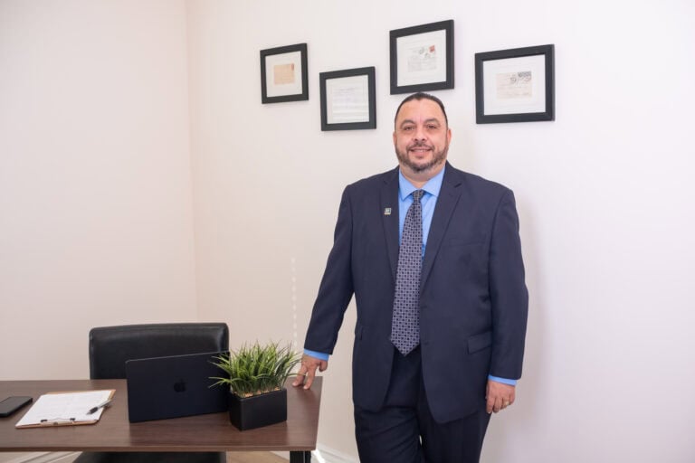 Professional Tony Tadros in business suit at an office desk, representing leadership and management.