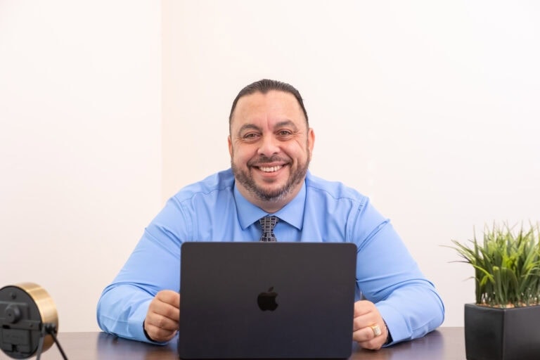 Smiling businessman with laptop in professional office, representing Tony Tadros.
