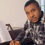 Homme togolais assis au piano avec partition ouverte.