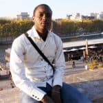 Jeune homme en chemise blanche avec vue sur la Seine et la ville de Paris.