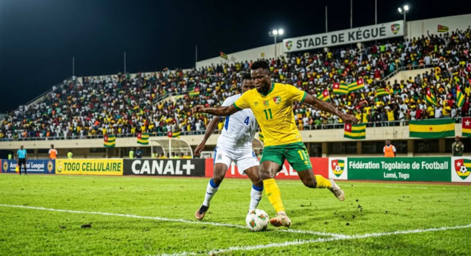 Match de football professionnel au Stade de Kégué à Lomé avec des joueurs en maillot jaune et vert.