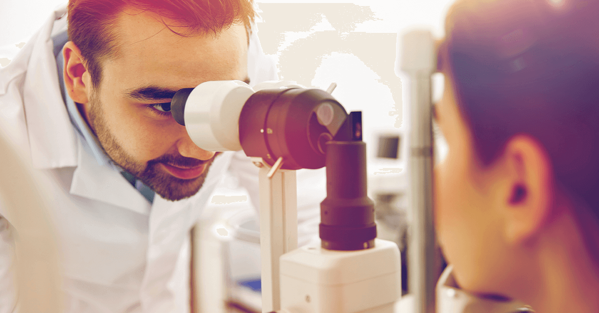An optometrist looking into a patient's eye with a slit lamp, symbolizing the detailed examination process that can now be enhanced or replaced by comfortable Optomap retinal imaging.