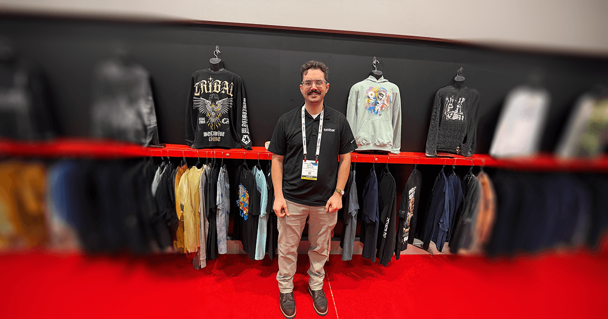 Matt standing in a trade show booth featuring printed apparel, symbolizing a successful career in the high-demand garment printing and creative trades.