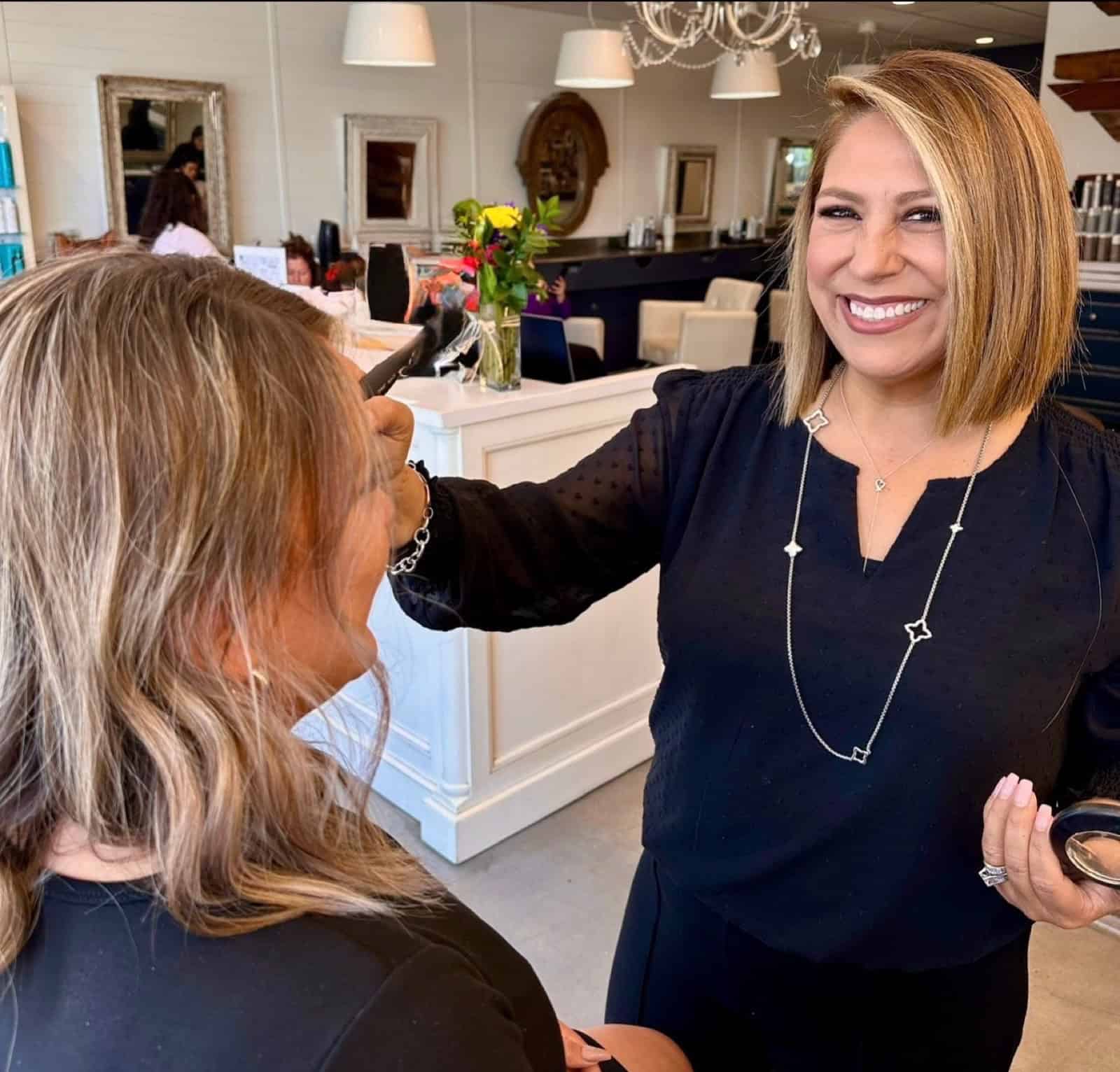 Laura, makeup artist and co-owner of The Dry Lounge in Yorba Linda, smiling while applying makeup to a client in her salon