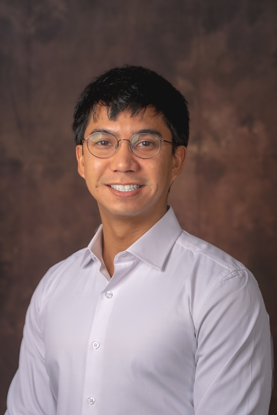 Tyler, a sports and surf photographer in San Diego, smiling in a white button-up shirt and round glasses in a studio headshot