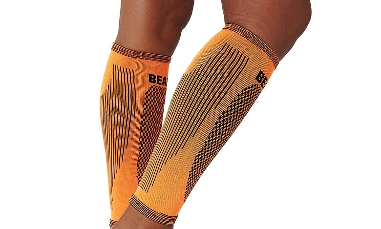 Orange compression leg sleeves on a runner's legs, showing athletic branding and patterns for tight fit and muscle support.
