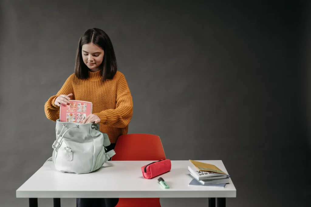 a student placing her notebook in a backpack