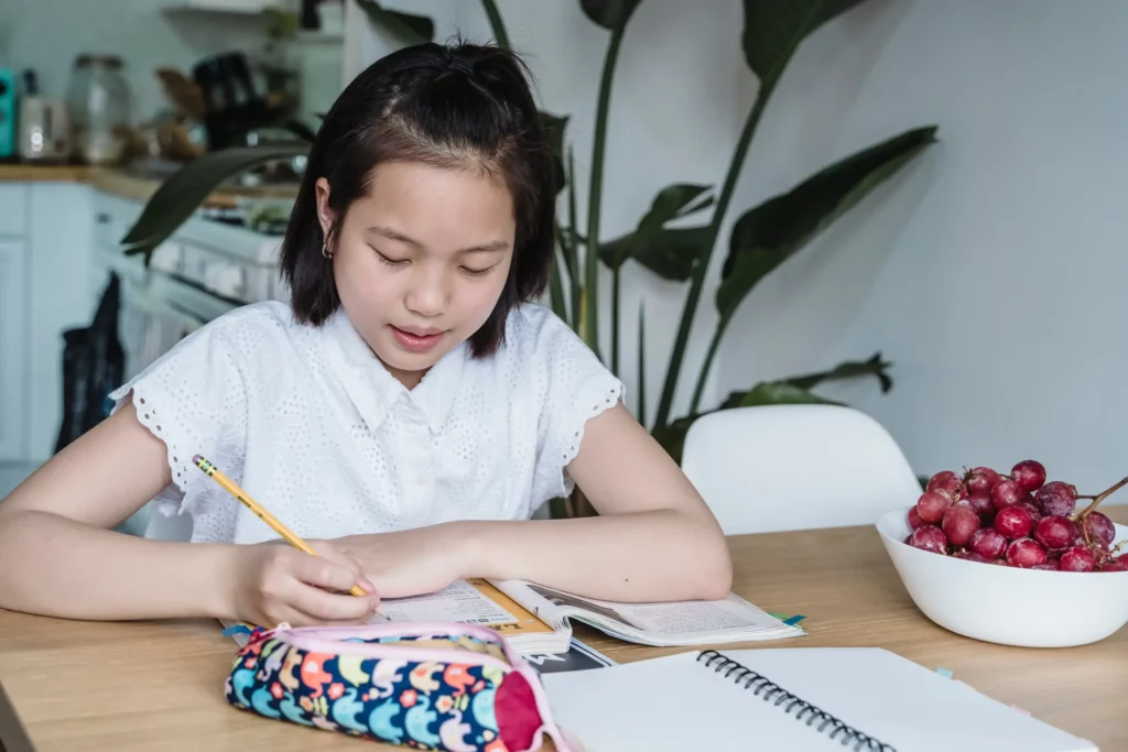 a girl in white top writing on a notebook