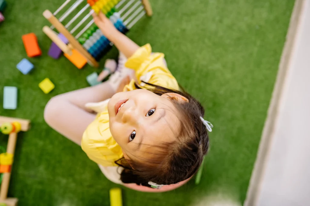 girl in a yellow dress looking up and smiling on camera while playing