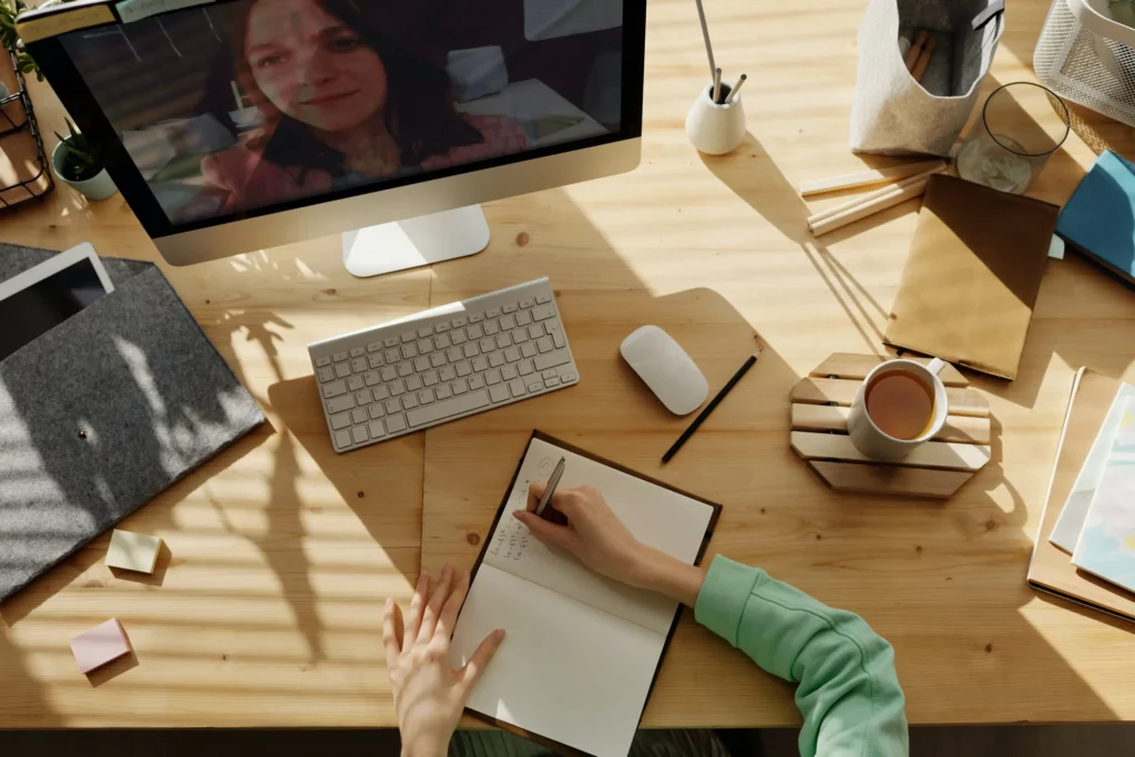 person writing on notebook while watching a documentary on computer screen