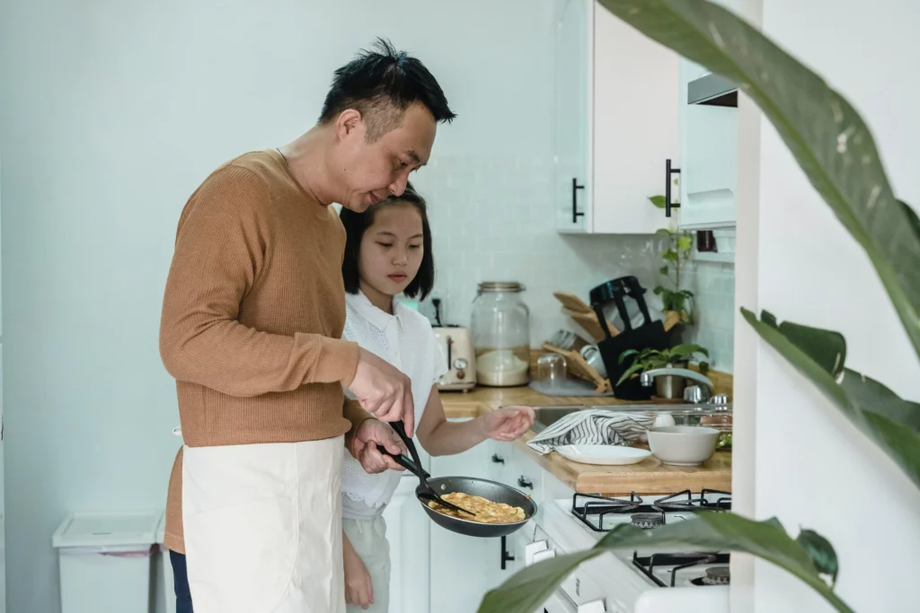 a dad teaching his daughter how to cook scrambled eggs
