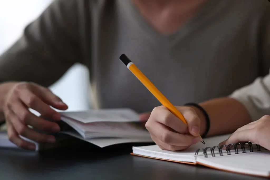 close up of a person writing in the notebook with pencil