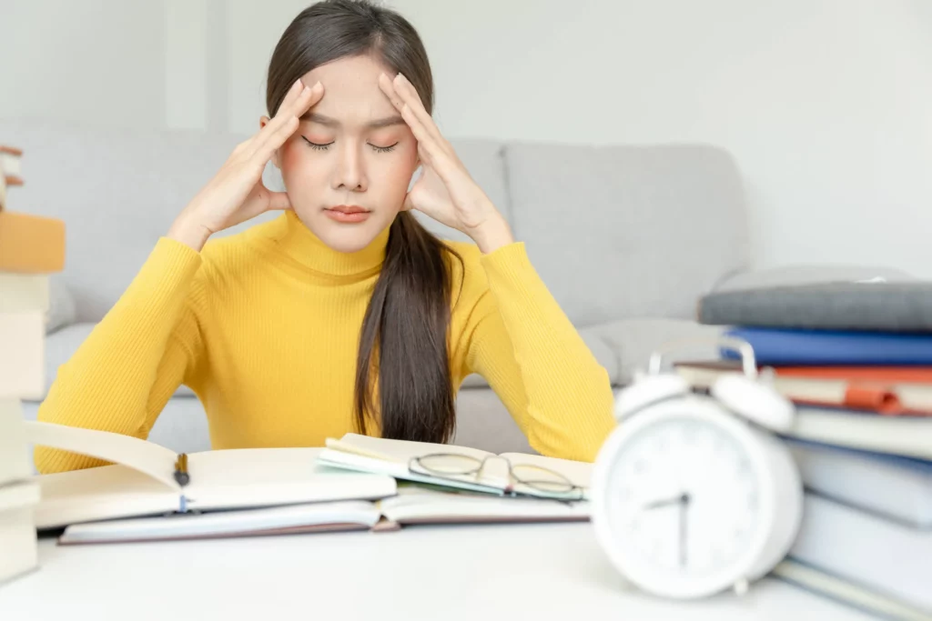 female student in a desk touching her forehead