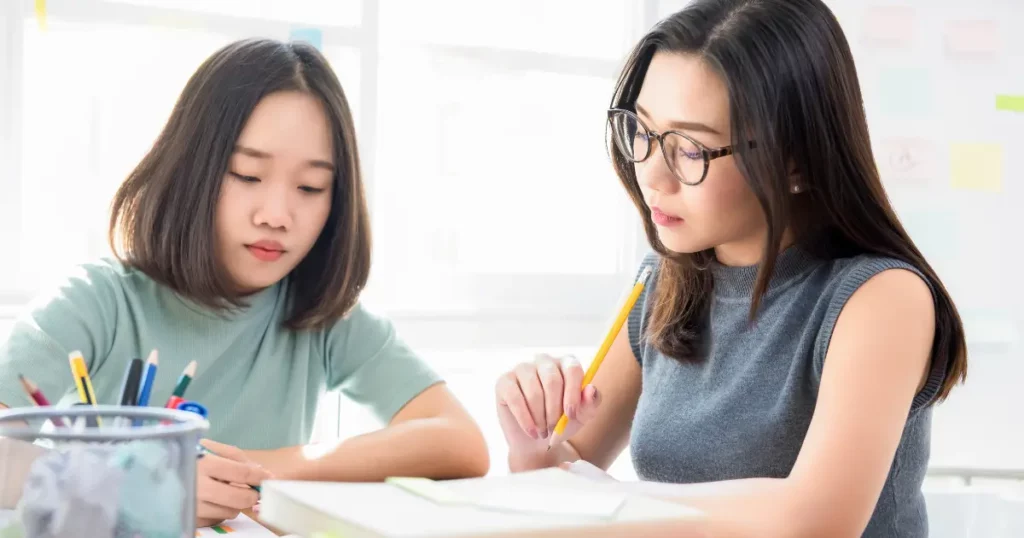 Two individuals sitting at a desk with books and pencils | tuitioncentre sg