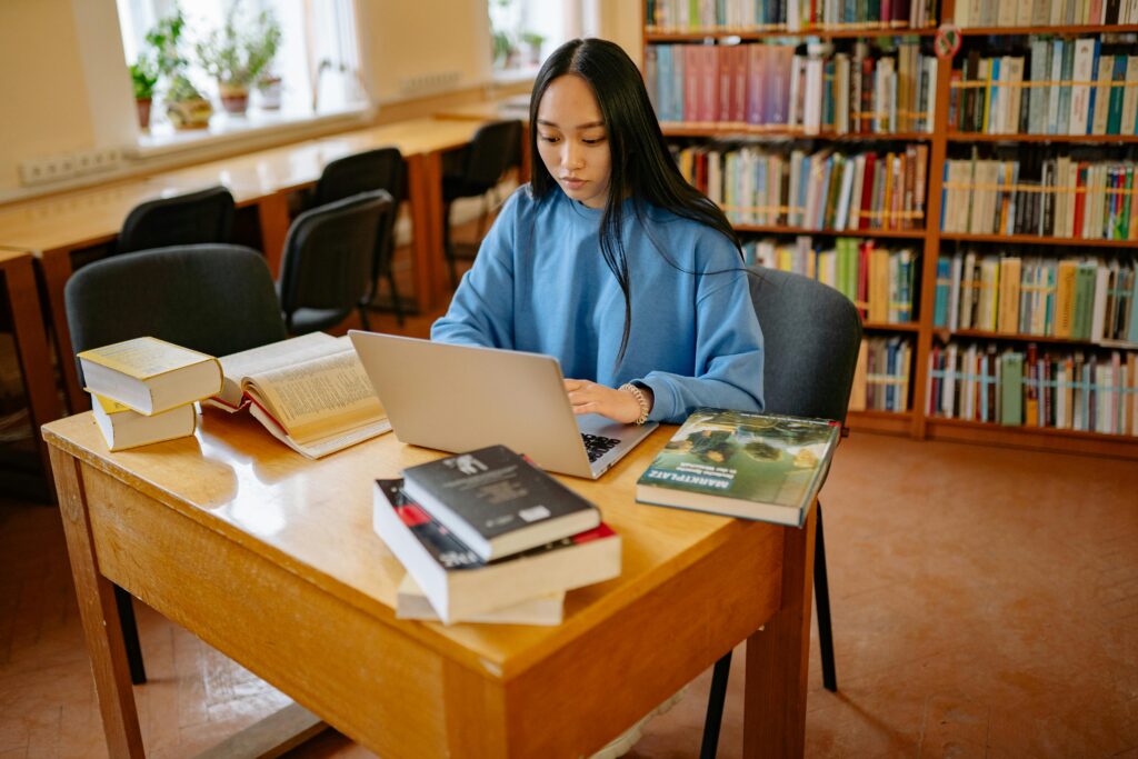 Woman in Blue Sweater Using Her Laptop in Library | Tuition Centre SG