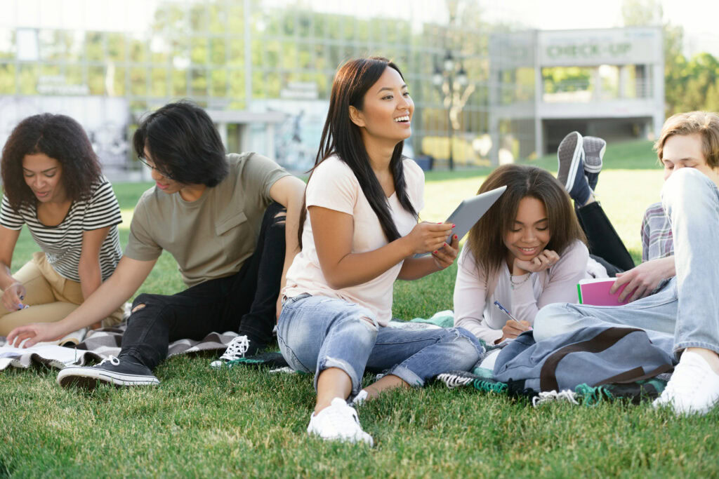 Photo of multiethnic group of young smiling students studying outdoors. Looking aside.