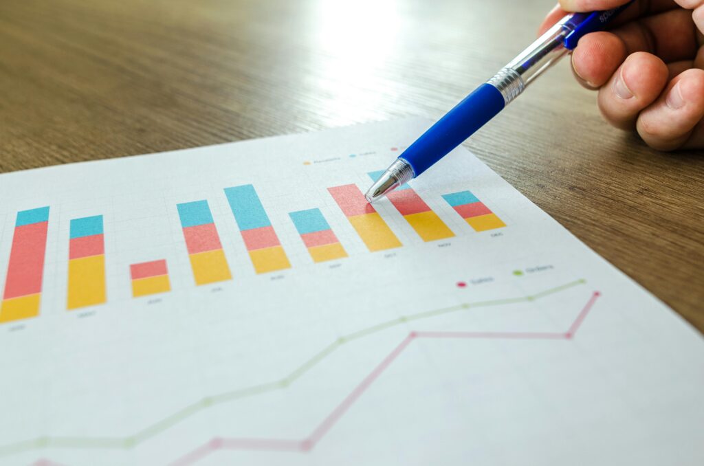 A hand points with a pen at a colourful bar and line graph on a sheet of paper on a wooden table. | TCS