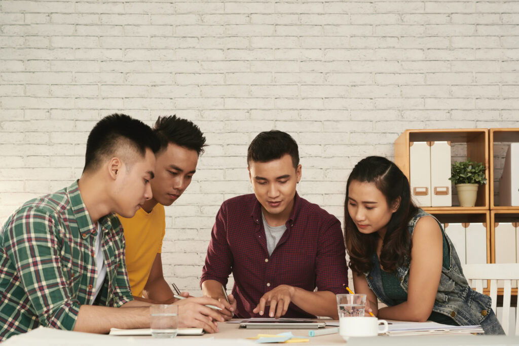 Four young adults sit at a table, collaborating and looking at documents in a modern office space. | TCS