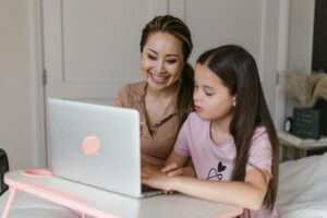 A woman and a girl smile whilst looking at a laptop together at a table in a cosy room. | TCS