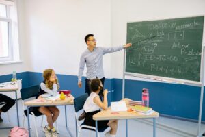 A teacher points at maths equations on a blackboard while pupils listen attentively in a classroom. | TCS