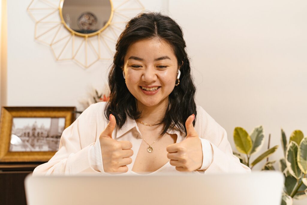 Woman smiling and giving two thumbs up whilst sitting in front of a laptop, wearing wireless earphones. | TCS