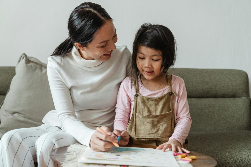 Woman and young girl sitting on a sofa, drawing together with coloured pencils and smiling. | TCS