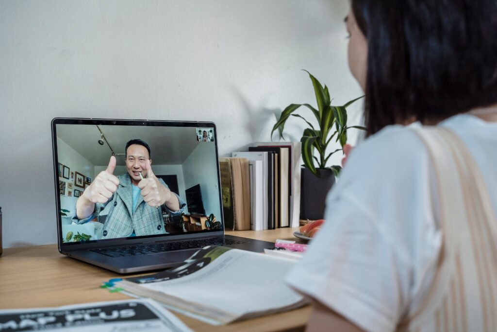 A person on a video call gives two thumbs up, while another studies the tuition methodology at a desk with books. | TCS