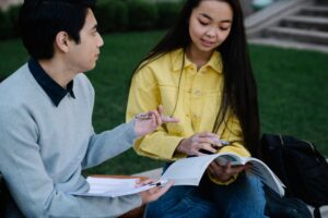 Two students sitting outside, studying together with books and notes in their hands. | TCS