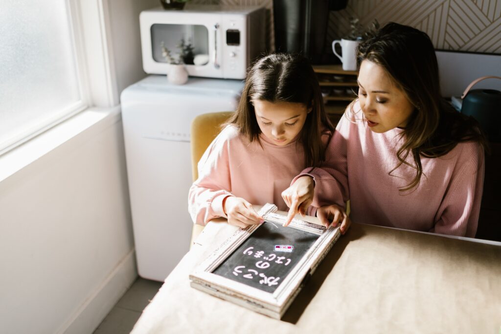 A woman and a girl work on maths problems together using a blackboard at a table in a bright kitchen. | TCS