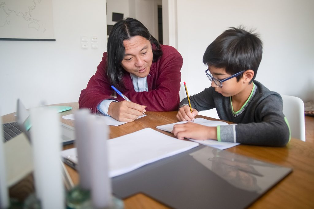 A tutor helps a young boy with homework at a table | TCS