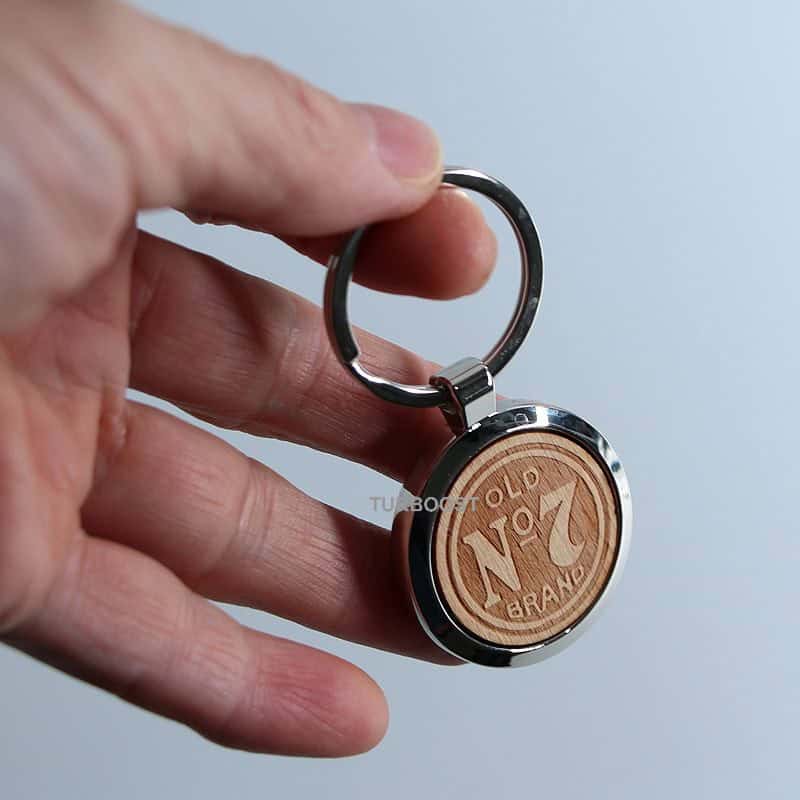 A round silver metal keychain with a wooden panel engraved with the text "OLD BRAND NO. 1" in the center, attached to a silver key ring.