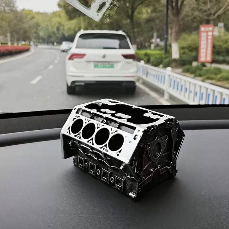 V8 engine model desktop organizer holding pens and business cards on a car dashboard.