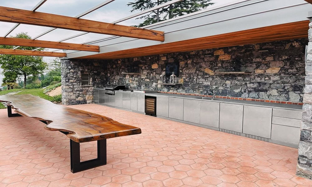 Outdoor kitchen with stone walls, stainless steel appliances, and wooden pergola.