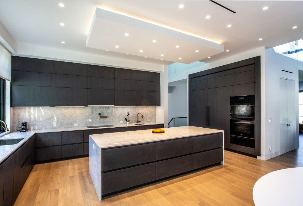 Italian kitchen in Tenafly, NJ, with black wood veneer Aster Cucine cabinetry, a large stone island, and integrated appliances.